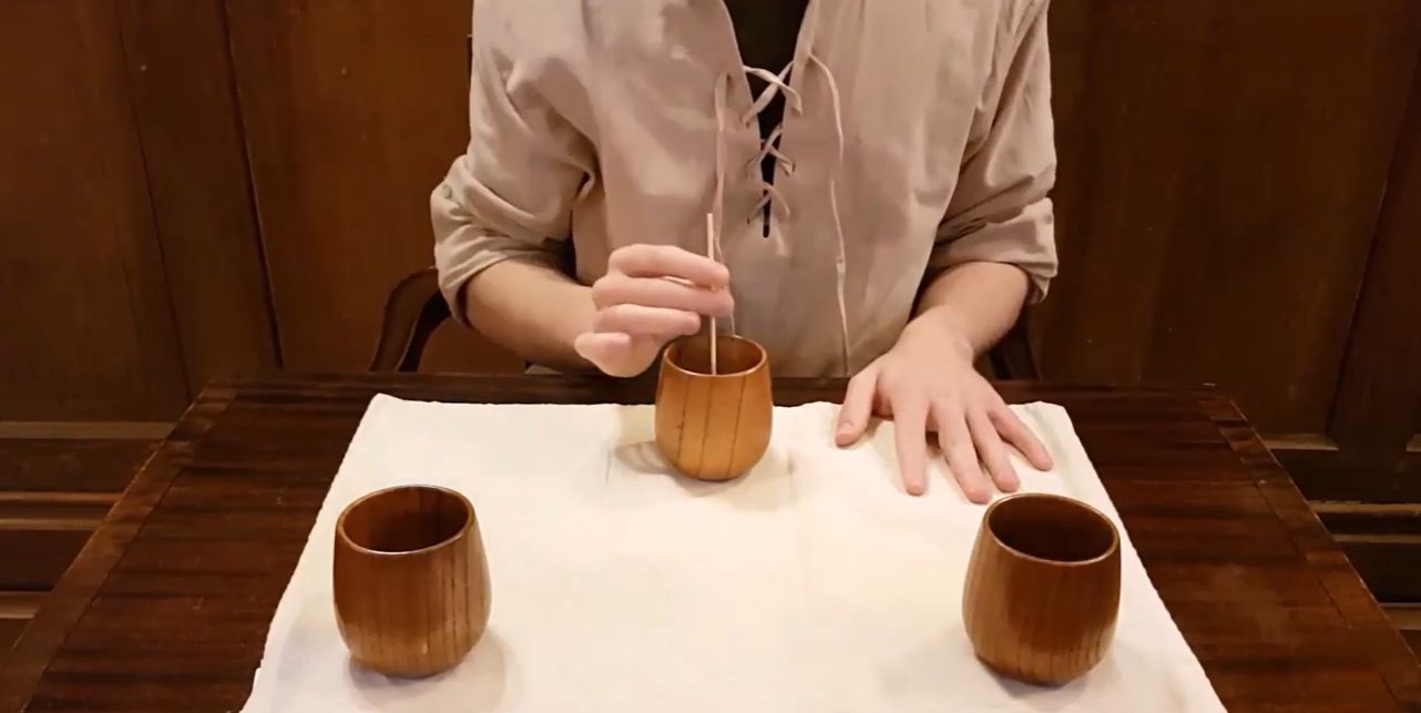 view showing the torso of a person in medieval dress at a table with wooden cups