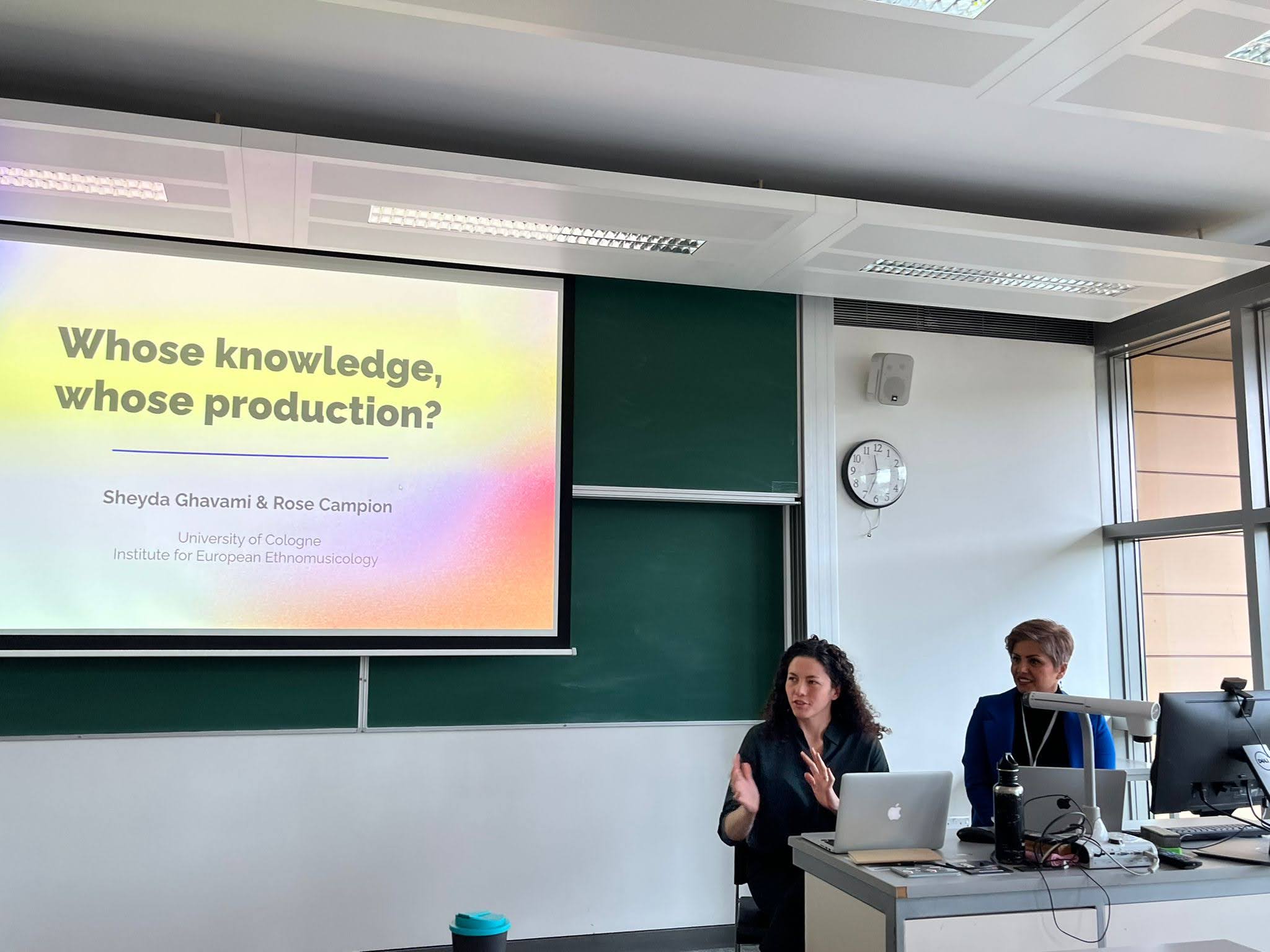 Two women at a desk with a powerpoint behind them