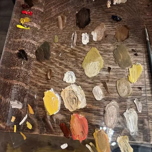 Smears of wet paint in browns and ochres on a wooden board with paintbrush