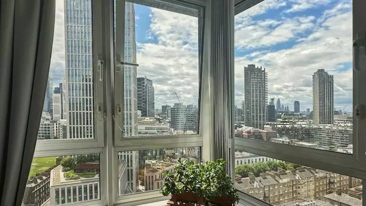 View from a living room's corner window showing sky scrapers and tower blocks on a sunny day