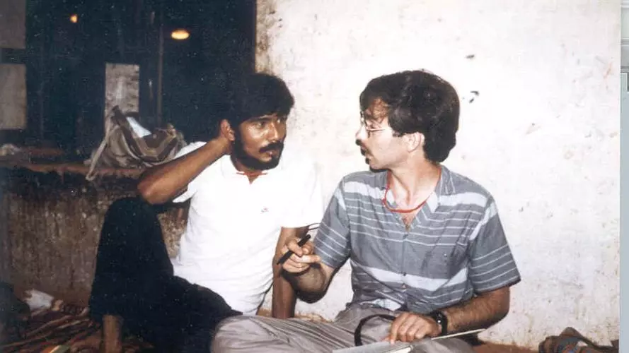 Two men seated cross legged on the floor in conversation