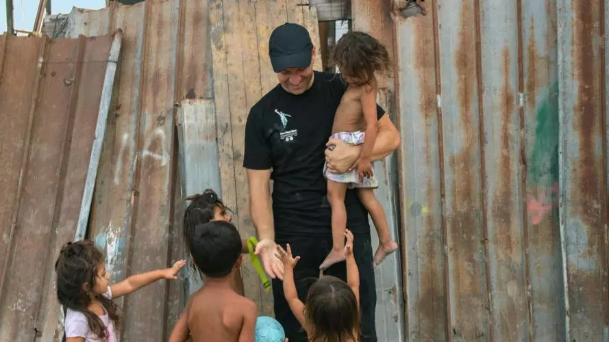 Gabriel carrying one child and playing with four others by broken down fence
