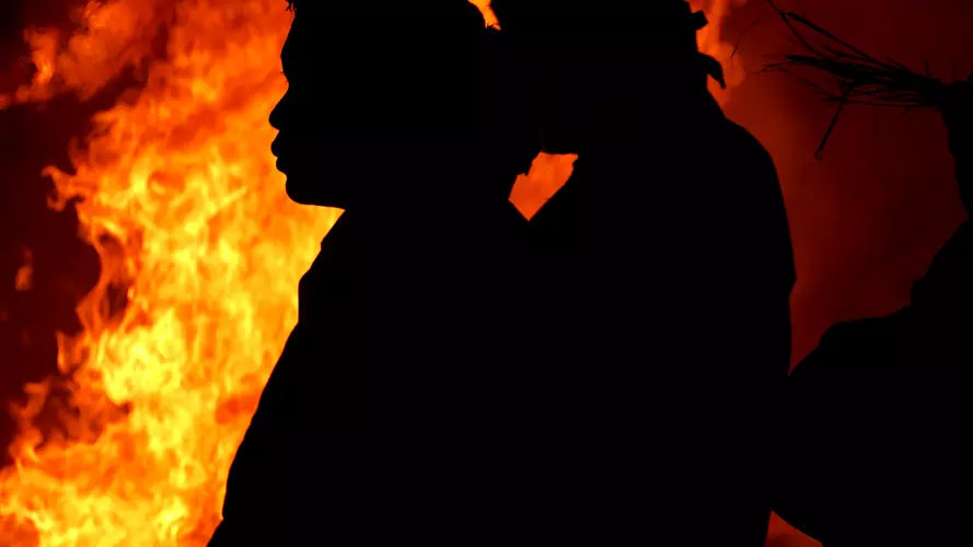 Figures in headdresses silhouetted against a large fire