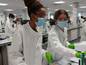 Two human sciences students at work in the lab wearing lab coats, face masks and gloves