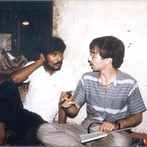 Two men seated cross legged on the floor in conversation