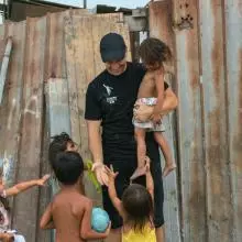 Gabriel carrying one child and playing with four others by broken down fence