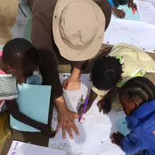 View of a group from above - children are drawing around a mans hand