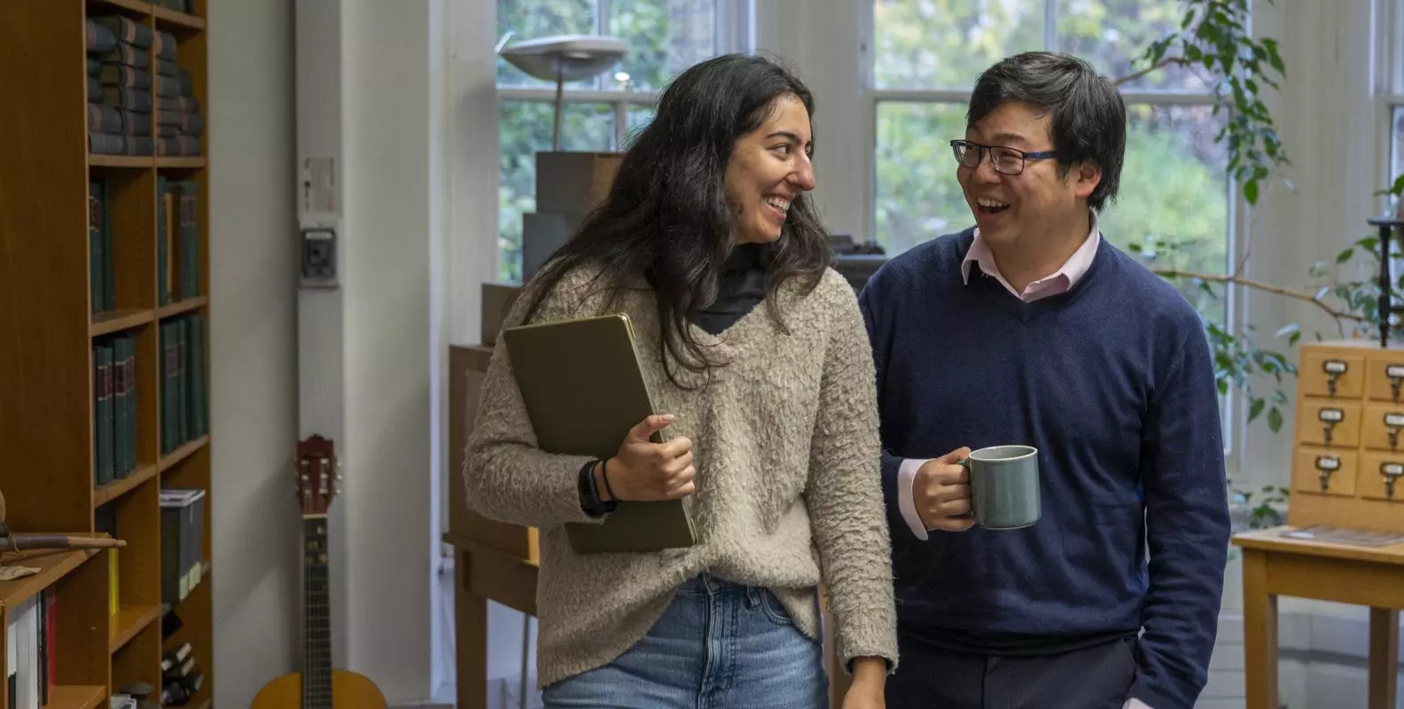a male and female students laughing with tea crop in front of a window