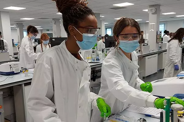 Two human sciences students at work in the lab wearing lab coats, face masks and gloves